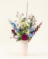Een witte vaas met het Zijden kunstbloemen boeket Purple Rain toont levendige paarse en witte kunstbloemen en groen blad, een toonbeeld van Nederlands vakmanschap tegen een lichte achtergrond.