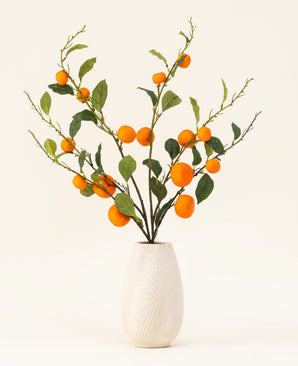 Het Zijden kunstbloemen boeket Mandarijn heeft een vaas met witte textuur en takken van groene bladeren en levendige oranje kunstmandarijnen, die een levendige toets geven tegen een effen lichte achtergrond.