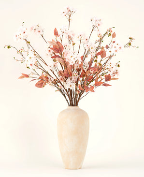 Een crèmekleurige vaas van keramiek bevat takken met delicate lichtroze Zijden kunstbloemen boeket Blushing Whisper en roodbruine bladeren tegen een effen achtergrond - ideaal voor elegante interieurs.