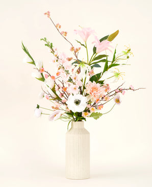 Een crèmekleurige vaas toont het Zijden kunstbloemen boeket Pink & Pearl, met delicate roze, witte en perzikkleurige zijden bloemen met groene bladeren tegen een licht neutrale achtergrond.