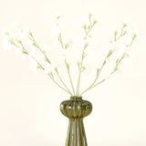 Een groene geribbelde glazen vaas bevat het Zijden kunstbloemen boeket Erwt crème met delicate witte zijden bloemen en slanke stelen, tegen een effen gebroken witte achtergrond.