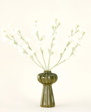 Een groene geribbelde glazen vaas bevat het Zijden kunstbloemen boeket Erwt crème met delicate witte zijden bloemen en slanke stelen, tegen een effen gebroken witte achtergrond.