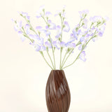 Een bruine, geribbelde vaas bevat het Zijden kunstbloemen boeket Erwt lavendel, met delicate bloemblaadjes en groene stelen tegen een effen gebroken witte achtergrond voor een subtiele cottage sfeer.
