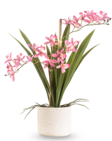 De Kunstplant Mini Cymbidium Real Touch 45 cm roze heeft lange groene bladeren en verschillende roze bloemstelen, gerangschikt in een eenvoudige pot met witte textuur en tegen een effen achtergrond.