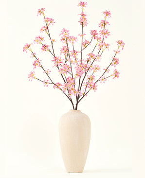 Een hoge vaas van beige keramiek bevat verschillende takken uit het Zijden kunstbloemen boeket Bloemen roze, met delicate roze bloesems en groene bladeren, tegen een effen witte achtergrond.