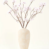 De Zijden kunstbloemen boeket Kersenbloesem lichtroze 114 cm staat in een hoge vaas van beige keramiek met lange, dunne takken en delicate lichtroze bloemen, waardoor een sereen kunstbloemen accent ontstaat tegen een effen achtergrond.