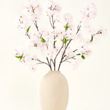 Het Zijden kunstbloemen boeket Kersenbloesem blush 119 cm toont delicate, lichtroze kersenbloesem met groene bladeren in een beige vaas, ideaal als kunstbloemen decoratie tegen een lichte achtergrond.