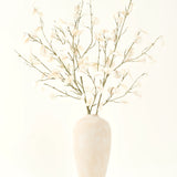 Het Zijden kunstbloemen boeket Eucalyptus crème in een hoge, lichtbeige keramische vaas met transparante witte bladeren zorgt voor een serene sfeer in elk kunstbloemen interieur tegen een lichte achtergrond.