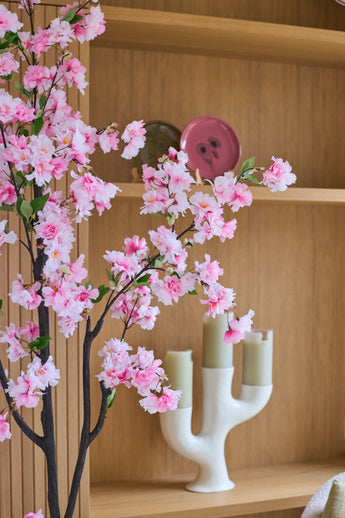 De ‘Kunst Kersenbloesem’ (150 cm) met roze takken is voor houten planken geplaatst, waarop groene kaarsen in een witte kandelaar en decoratieve borden staan uitgestald.