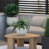 Op een klein vloerkleed naast een grijze bank op een terras staat een houten salontafel met daarop een Kunstplant Bird’s Deluxe van 60 cm, met op de achtergrond nog enkele potplanten.