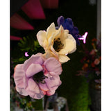 Close-up van Kunstanemoon Real Touch Blauw Paars 52cm kunstbloemen - lavendel, crème en blauw - tegen een vage achtergrond van groen, kleurrijke bloemen en roze neonverlichting.