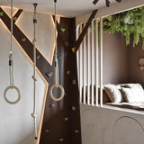Een moderne kinderspeelkamer heeft een klimwand, gymringen, touw en een gezellige leeshoek met kussens en verticale latten. Kunsthaag Lush Deco Deluxe 100x100 cm UV voegt groen toe aan het plafond en vult de neutrale tinten en speelse verlichting van de kamer aan.