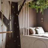 Een gezellige kinderslaapkamer met een ingebouwd bed en kussens is versierd met de Kunsthaag Lush Deco Deluxe 100x100 cm UV, die weelderig groen toevoegt. Een klimmuur, touwladder en schommel creëren een boomhutgevoel bij daglicht.