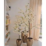 Drie Kunstplant Bougainvillea van 180 cm lang, elk in een pot met gouden textuur, worden in een zonovergoten kamer geplaatst met beige gordijnen en een boekenplank, waardoor een elegante en lichte sfeer binnenshuis wordt gecreëerd.