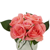 De Kunstrozenboeket Real Touch Roze 18cm heeft vijf roze kunstrozen met groene bladeren, dicht op elkaar in een kleine glazen vaas met water, tegen een witte achtergrond.