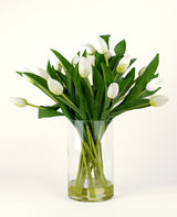 Het Zijden kunstboeket Tulpen in vaas Wit heeft witte tulpen met groene bladeren en stelen in een heldere glazen vaas, tegen een eenvoudige lichte achtergrond.