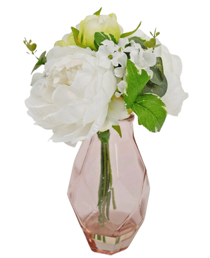 Het Kunstboeket in glas 25 cm heeft een klein boeket van witte bloemen met groene bladeren, gerangschikt in een facetgeslepen, lichtroze glazen vaas.