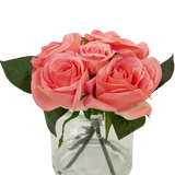 De Kunstrozenboeket Real Touch Roze 18cm heeft kleine roze kunstrozen met groene bladeren in een heldere glazen pot tegen een witte achtergrond.